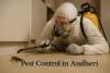 Pest control worker in Andheri spraying pesticide on cockroach under furniture wearing protective gear and yellow sprayer.